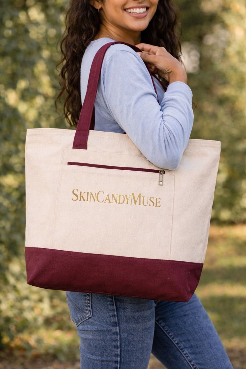 Woman outdoors smiling with a SkinCandyMuse canvas tote bag with maroon accents
